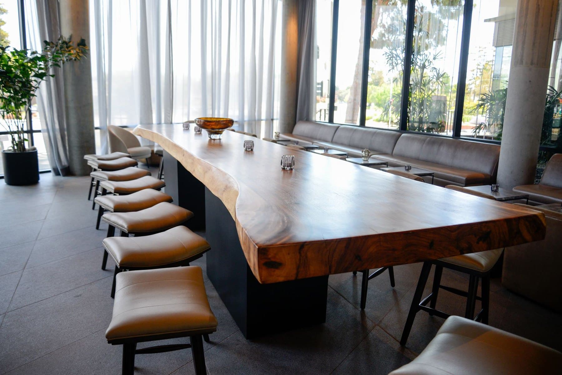 A long live-edge wooden meeting table lined with chairs beside a wall of windows