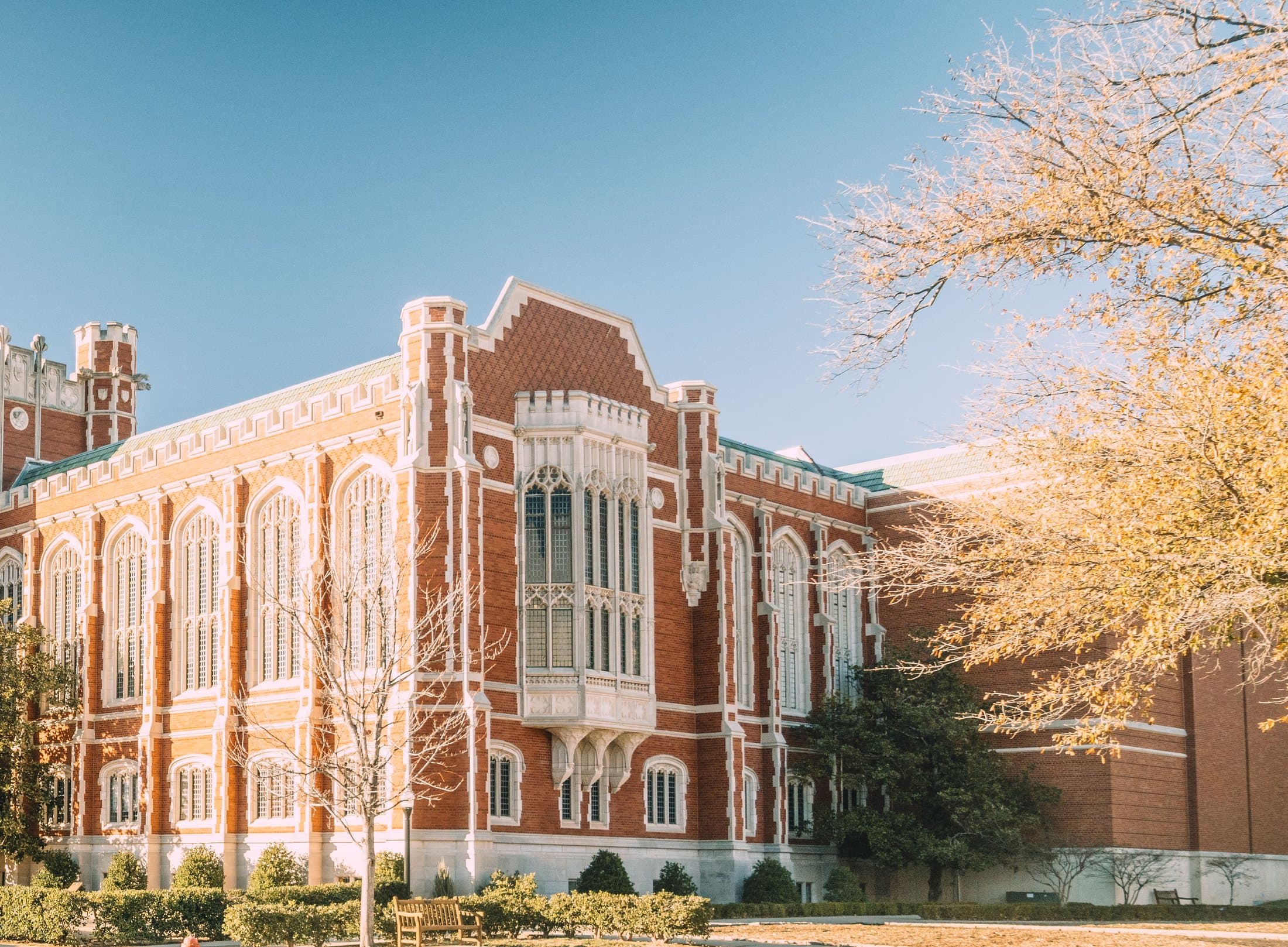 A Gothic revival collegiate hall in red brick and pale stone, with a golden autumn tree beside it