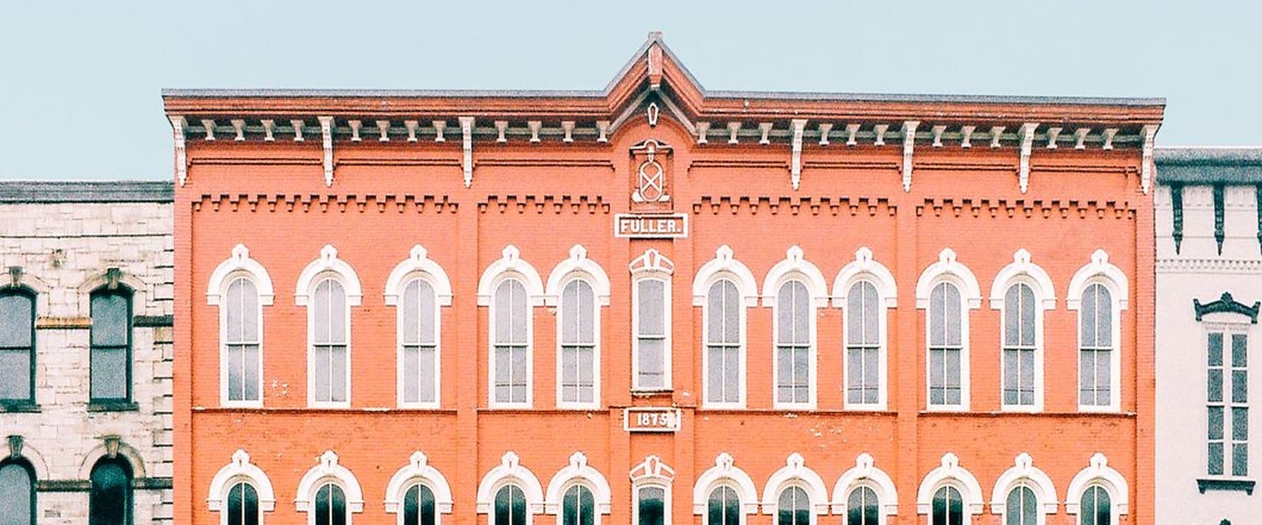 The brick facade of a main street commercial building dated 1875, with rows of arched windows