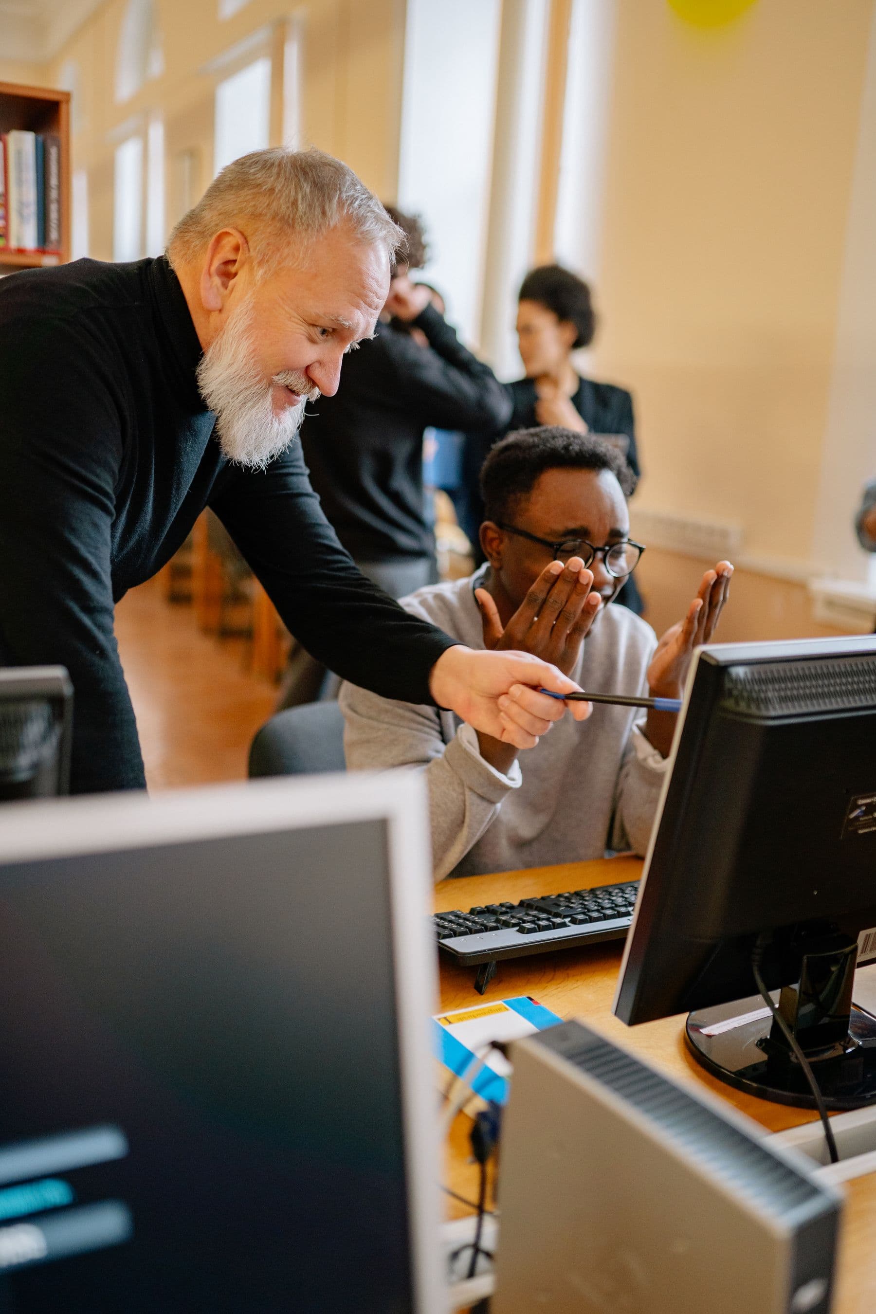 An experienced advisor guiding a younger colleague through work at a computer