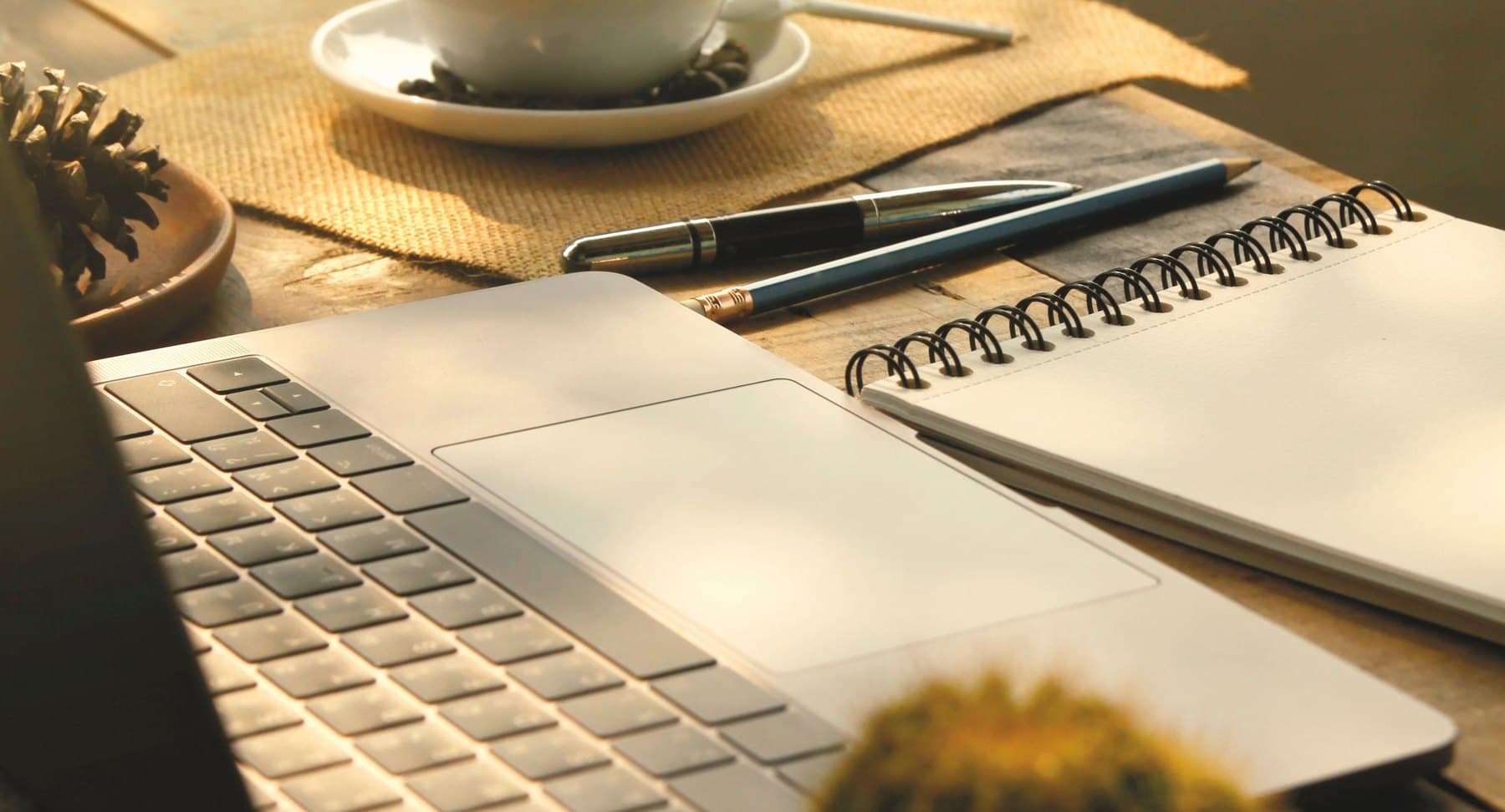 An open notebook and pen beside a cup of coffee on a sunlit table