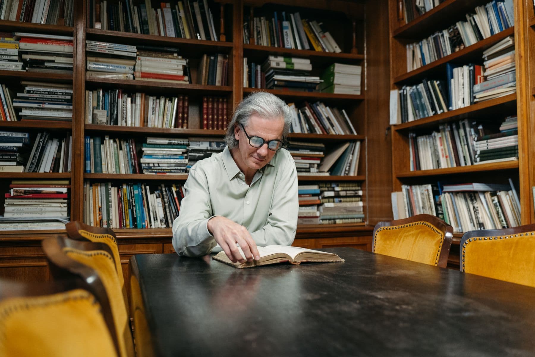 An older man reading in a warm library lined with wooden bookshelves