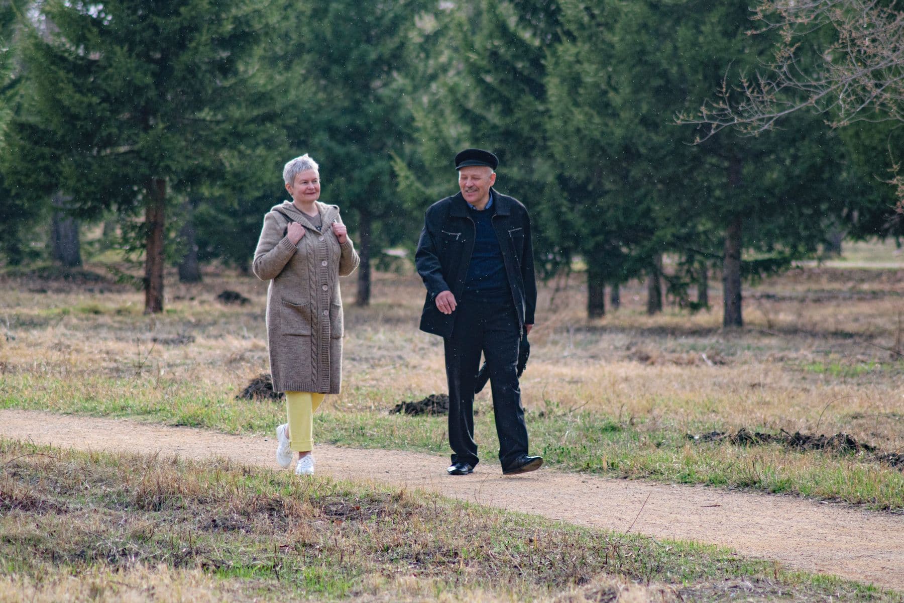 A smiling older couple walking together along a tree-lined park path on a bright spring day