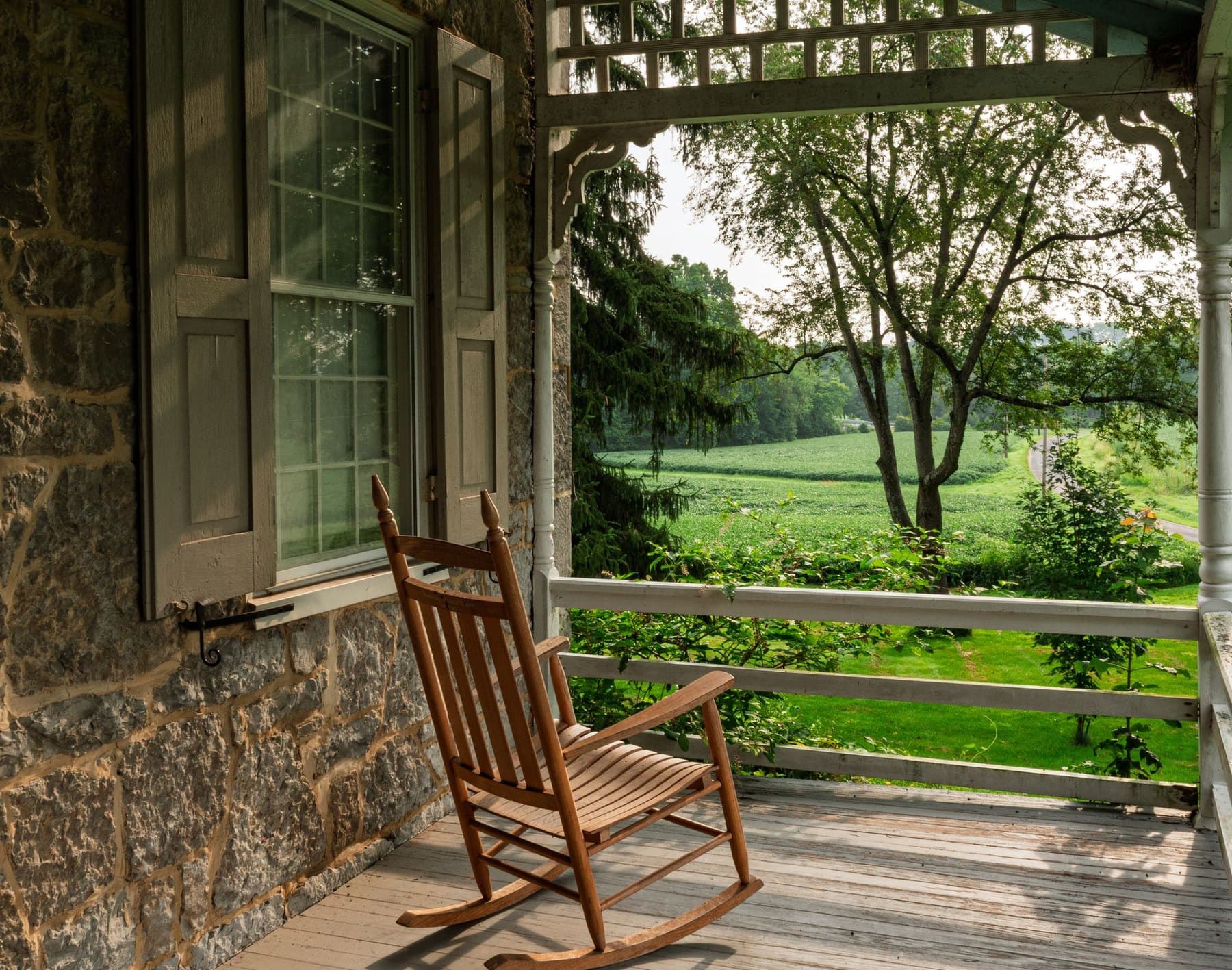 A wooden rocking chair on a stone porch looking out across a green summer field