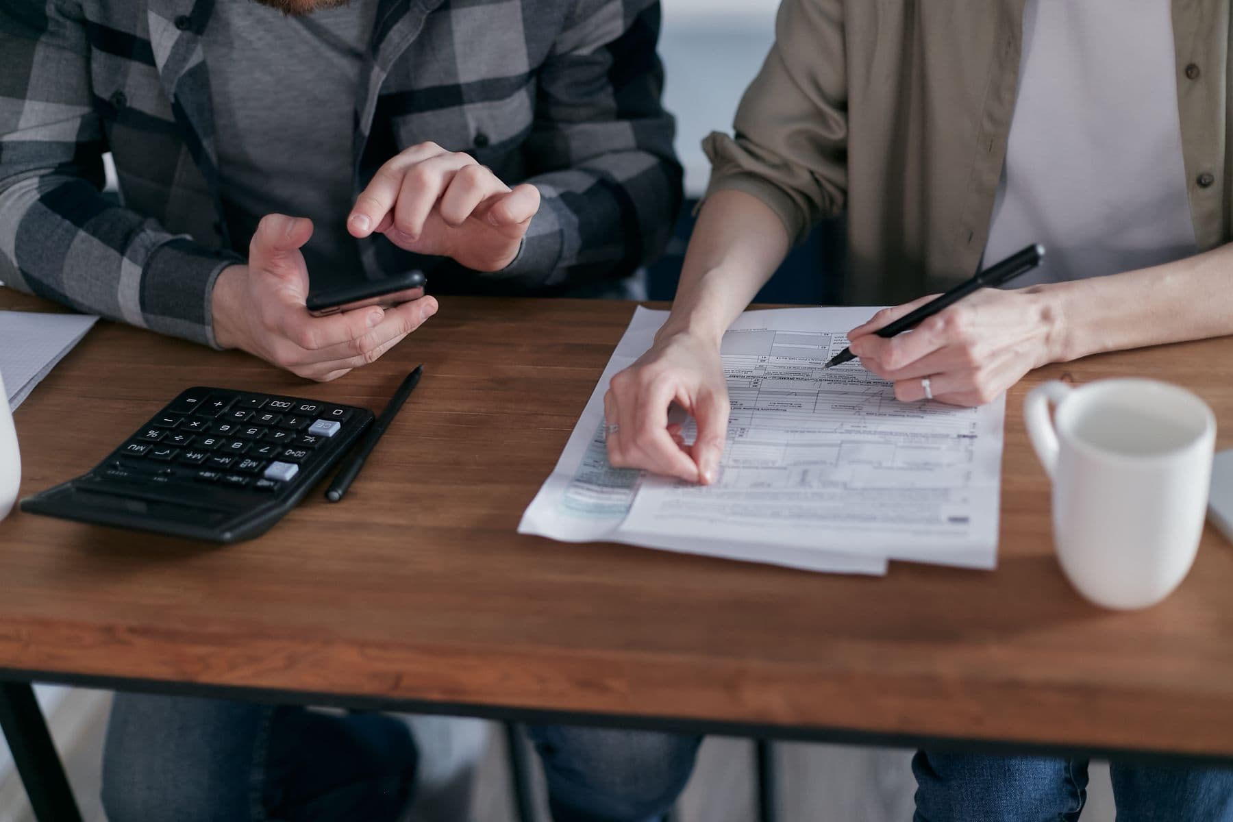 Two people reviewing tax forms together at a wooden desk with a calculator