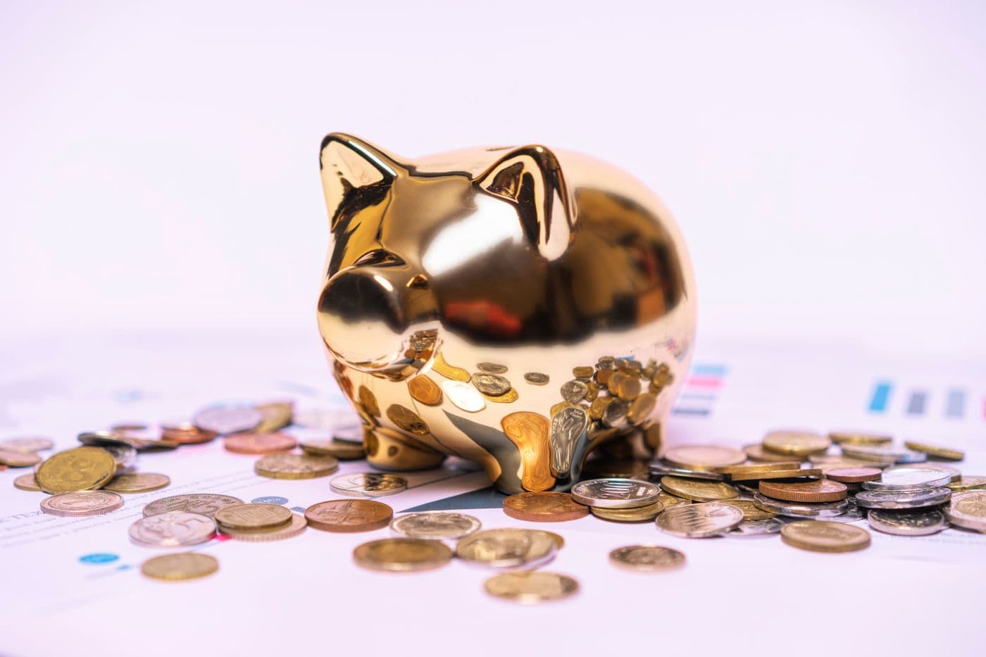 A piggy bank resting on financial documents with scattered coins