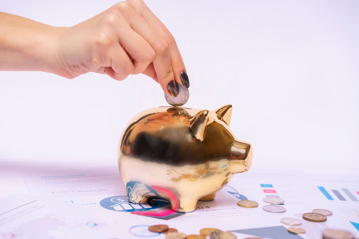 A hand placing a coin into a piggy bank beside financial paperwork